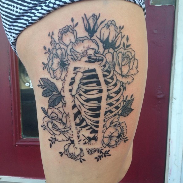 Unusual black and white human chest bones with transparent coffin tattoo on thigh stylized with various flowers
