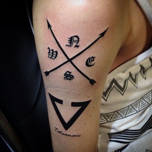Unusual combined black in crossed arrows with various symbols tattoo on shoulder stylized with lettering