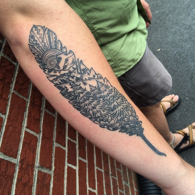 Unusual feather shaped tattoo on forearm stylized with mountain forest