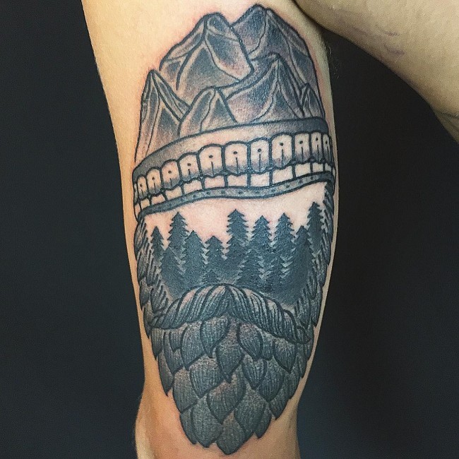 Unusual shaped black ink old forest tattoo on arm with mountains