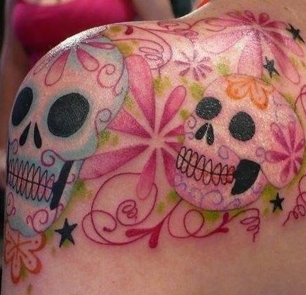 Usual cartoon style colored Mexican traditional skulls tattoo on shoulder stylized with beautiful flowers and stars
