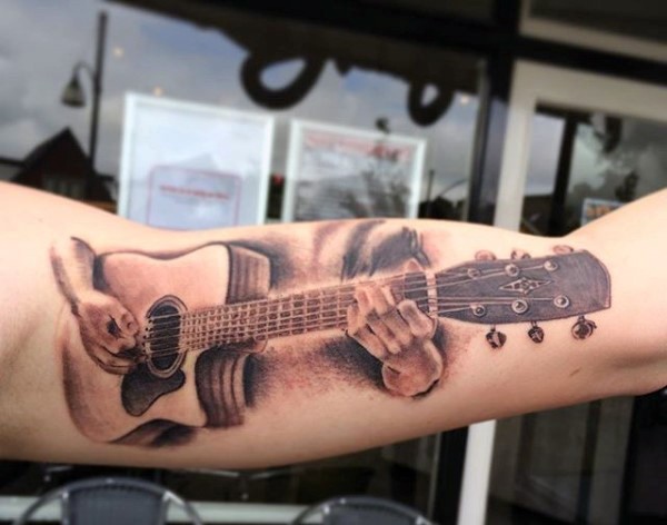 Tatuaje en el brazo, músico que toca la guitarra acústica
