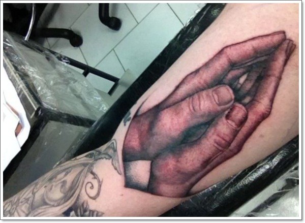 Very realistic painted and colored praying hands tattoo on arm