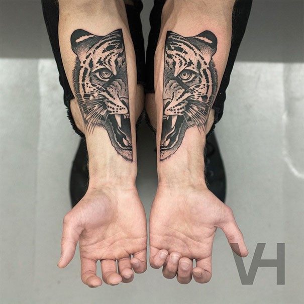 Very symmetrical looking black ink forearm tattoo of split roaring tiger head