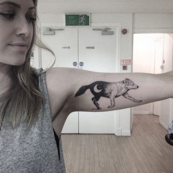 Walking wolf decorated with new Moon black and white tattoo on lady's biceps