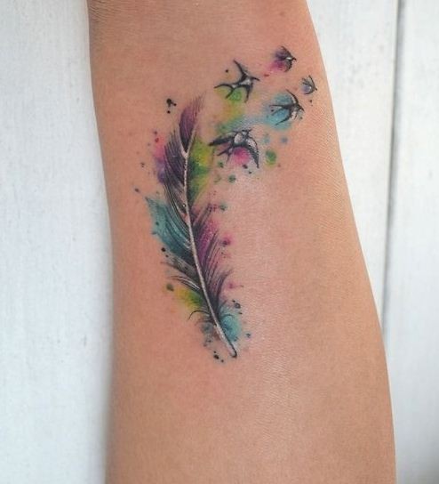 Tatuaje en el antebrazo,
pluma multicolor con aves diminutos
