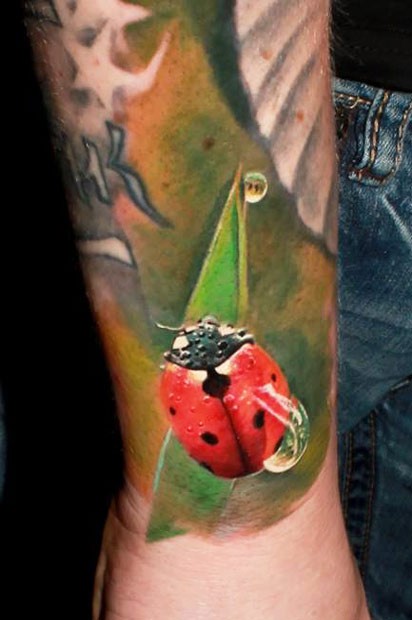 Tatuaggio bellissimo colorato sul braccio la coccinella con la rugiada