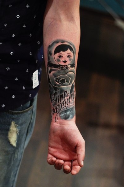 Watercolor style colored forearm tattoo of Matryoska doll with lettering