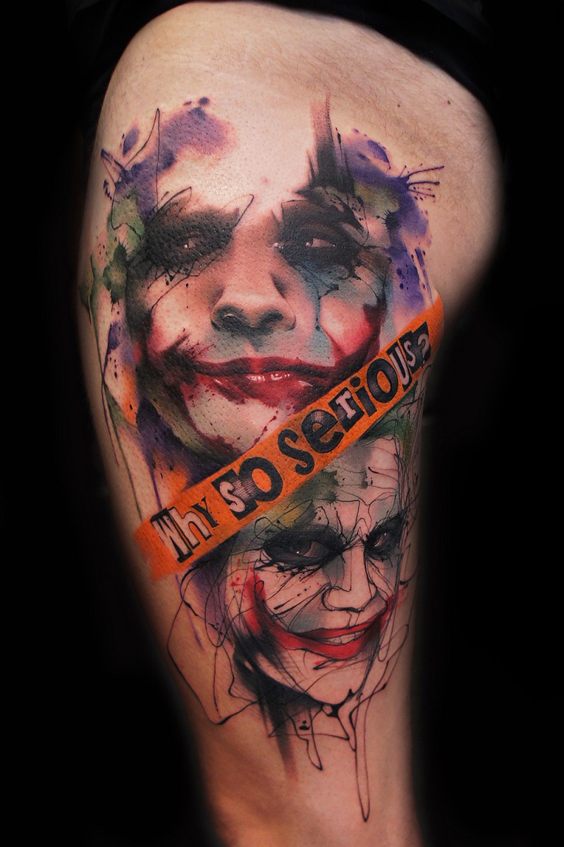 Watercolor style colored thigh tattoo of Joker face with lettering