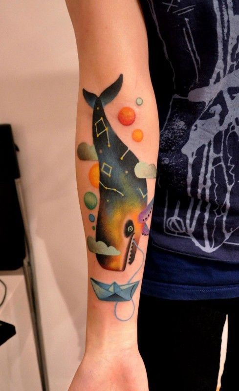 Tatuaje en el antebrazo, dibujo abstracto de ballena entre planetas y barco de papel